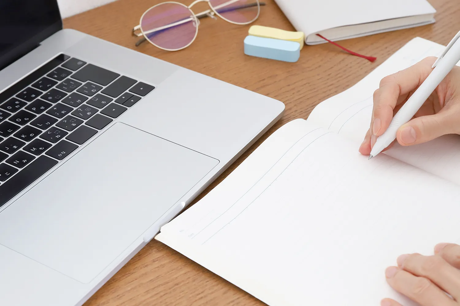 パソコンの前でノートに何かを書く写真