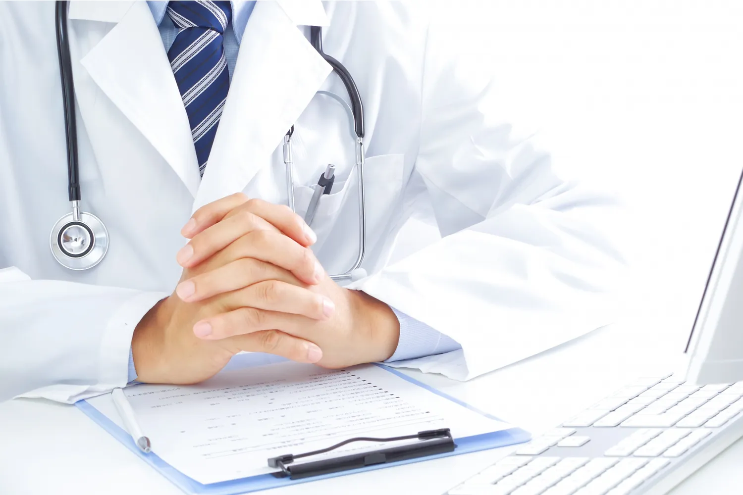 パソコンの前で聴診器をかけて診断書を見る医師の写真
