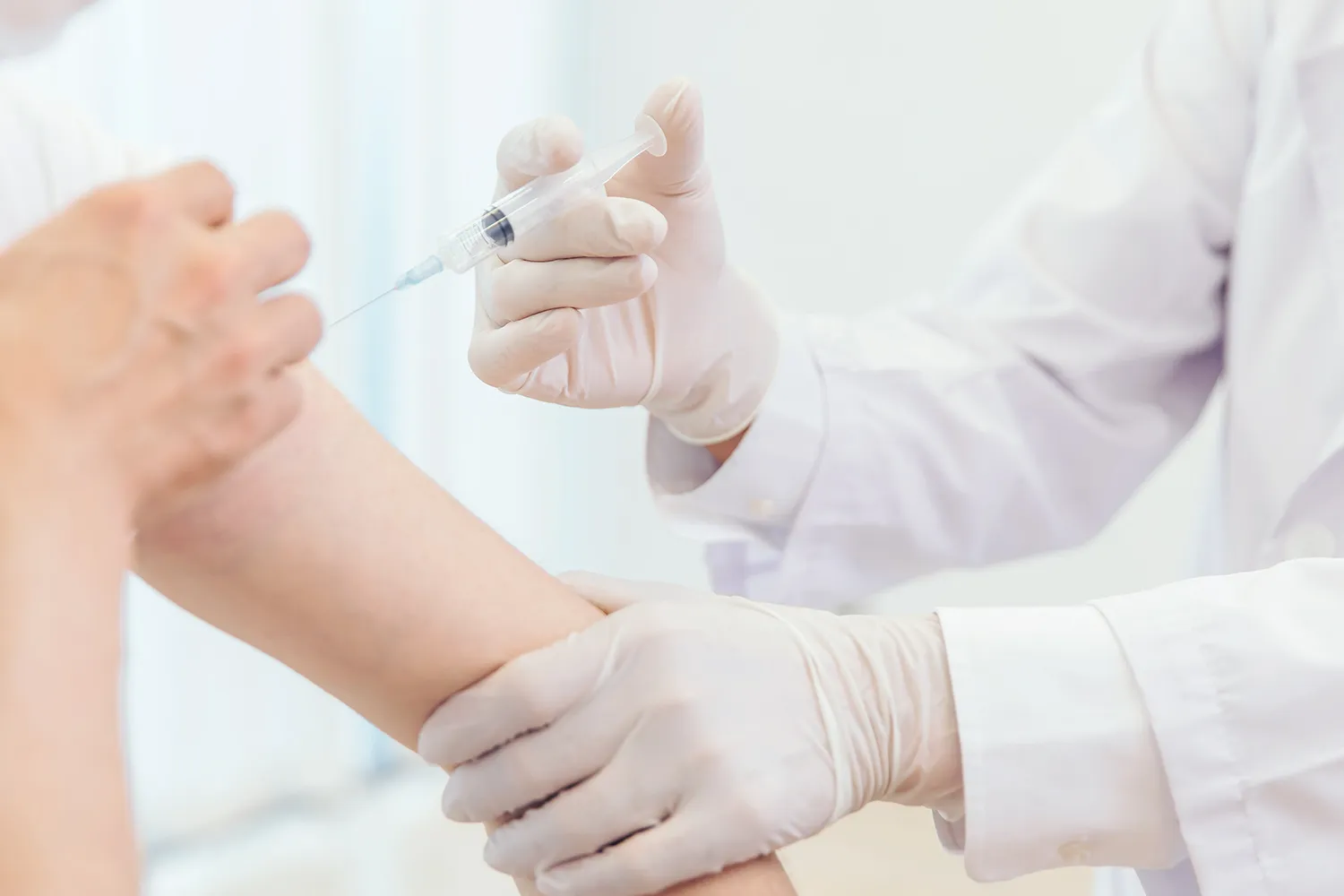 腕まくりした人の腕に注射を打つ医療関係者の写真
