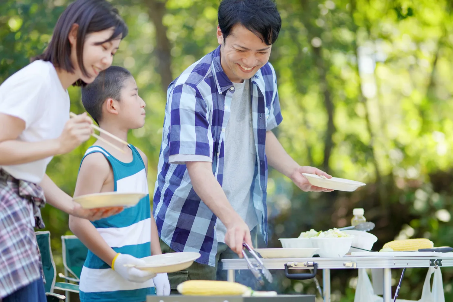 キャンプでバーベキューする家族の写真