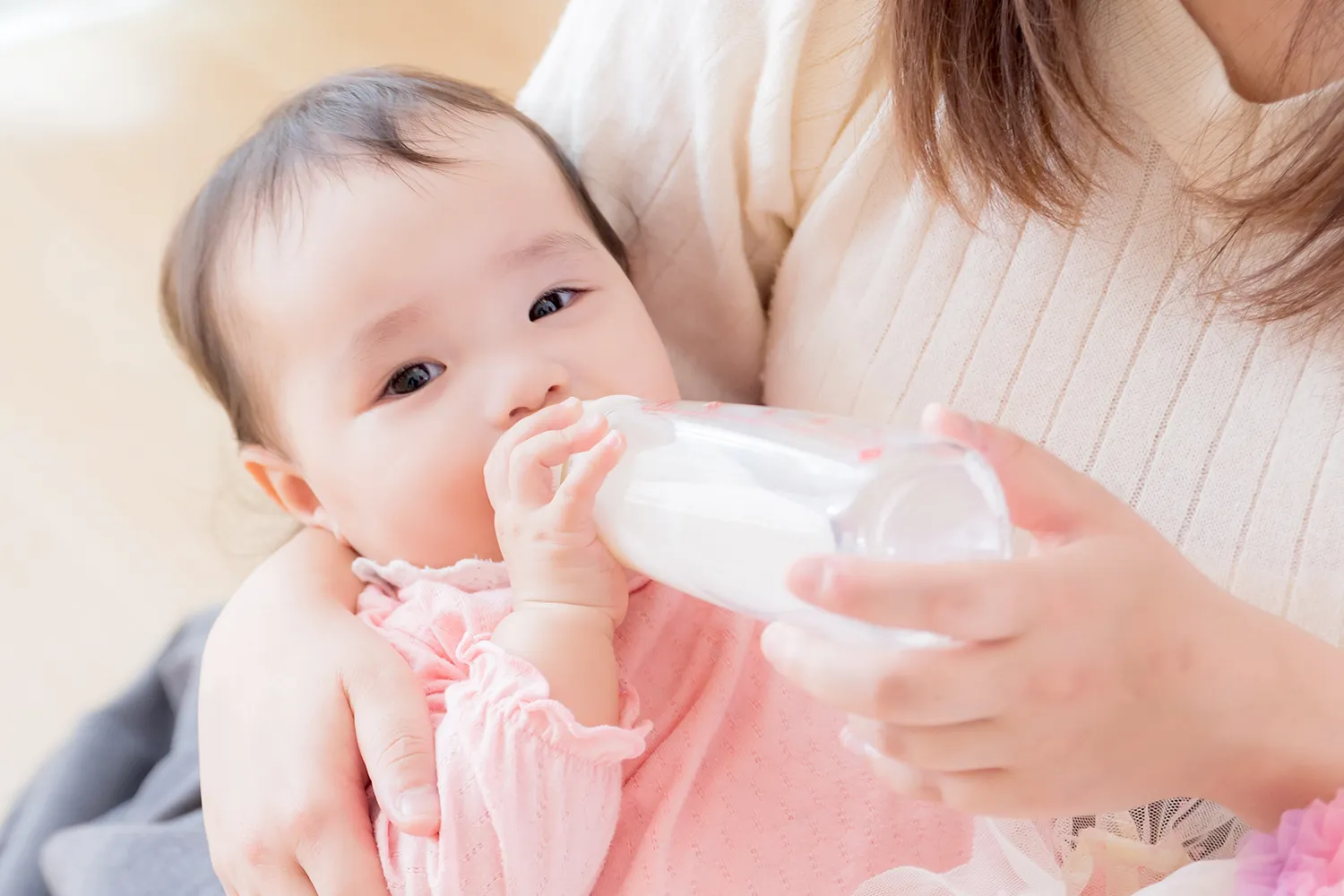母親に抱っこされて哺乳瓶のミルクを飲む赤ちゃんの写真
