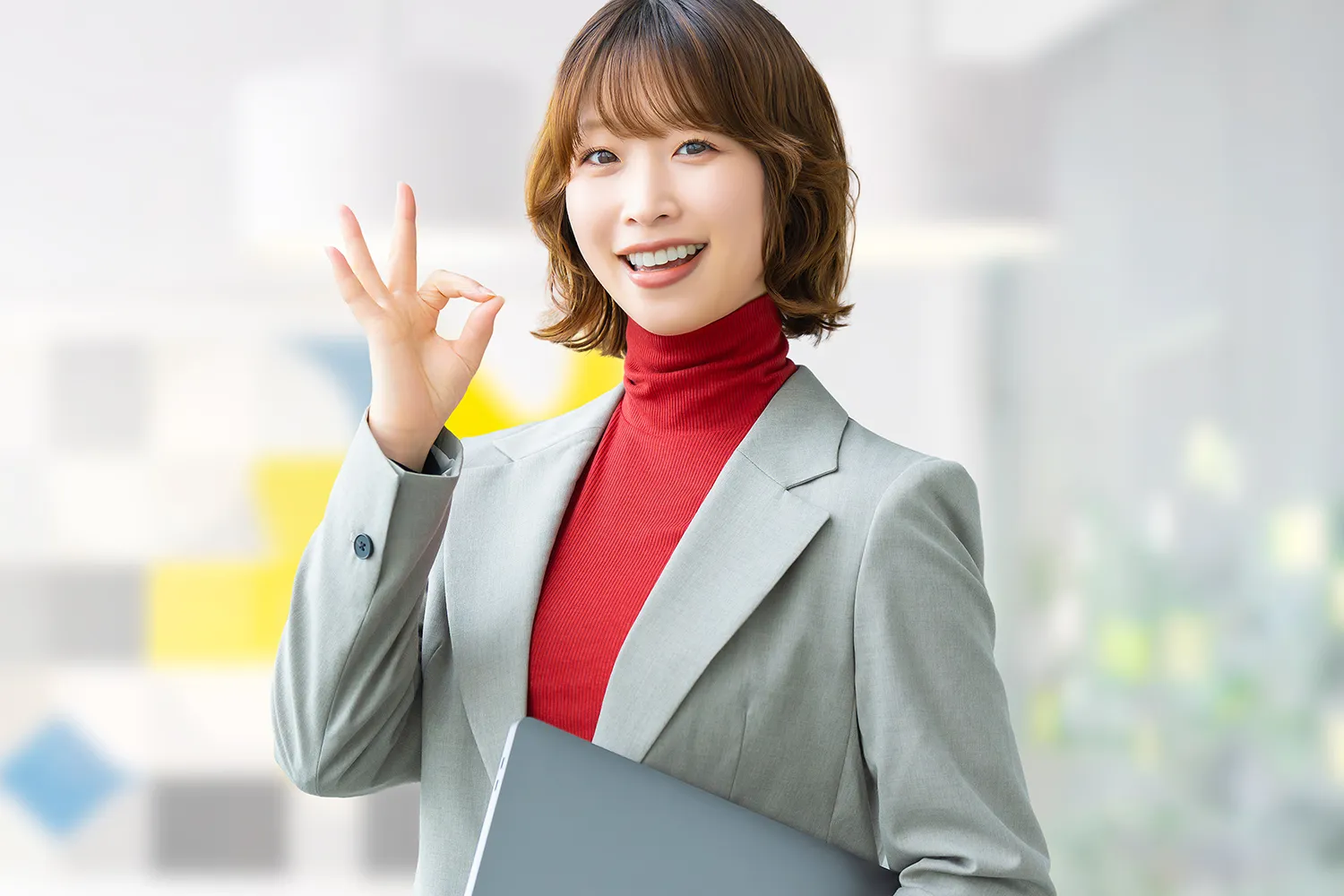 OKサインを出すノートパソコンを持ったキャリアウーマンの写真