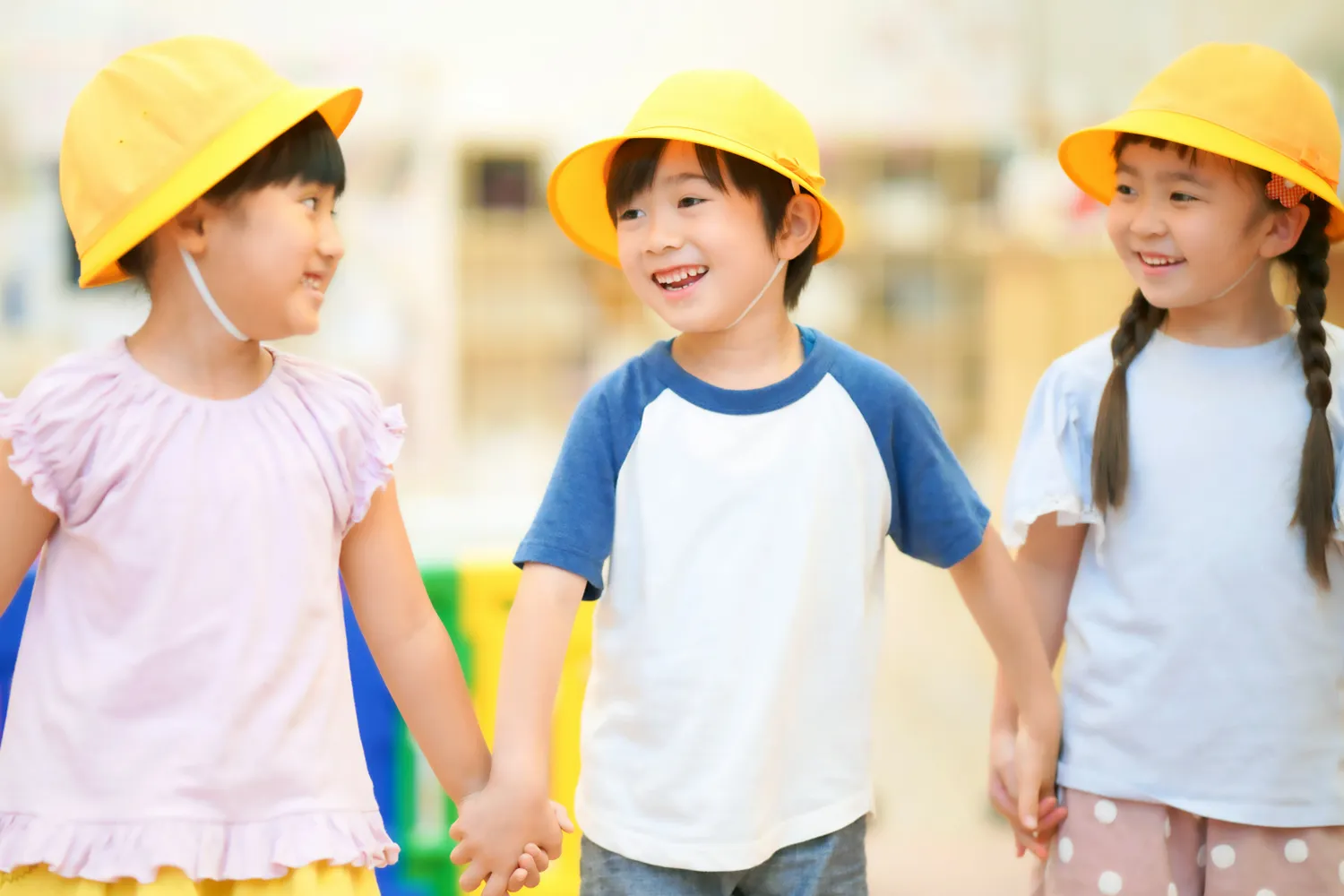 手をつなぐ黄色い帽子の園児3人の写真